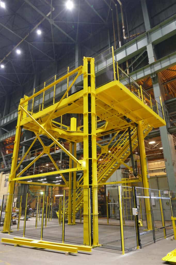 A large yellow four-post vertical lift system within an industrial workshop.