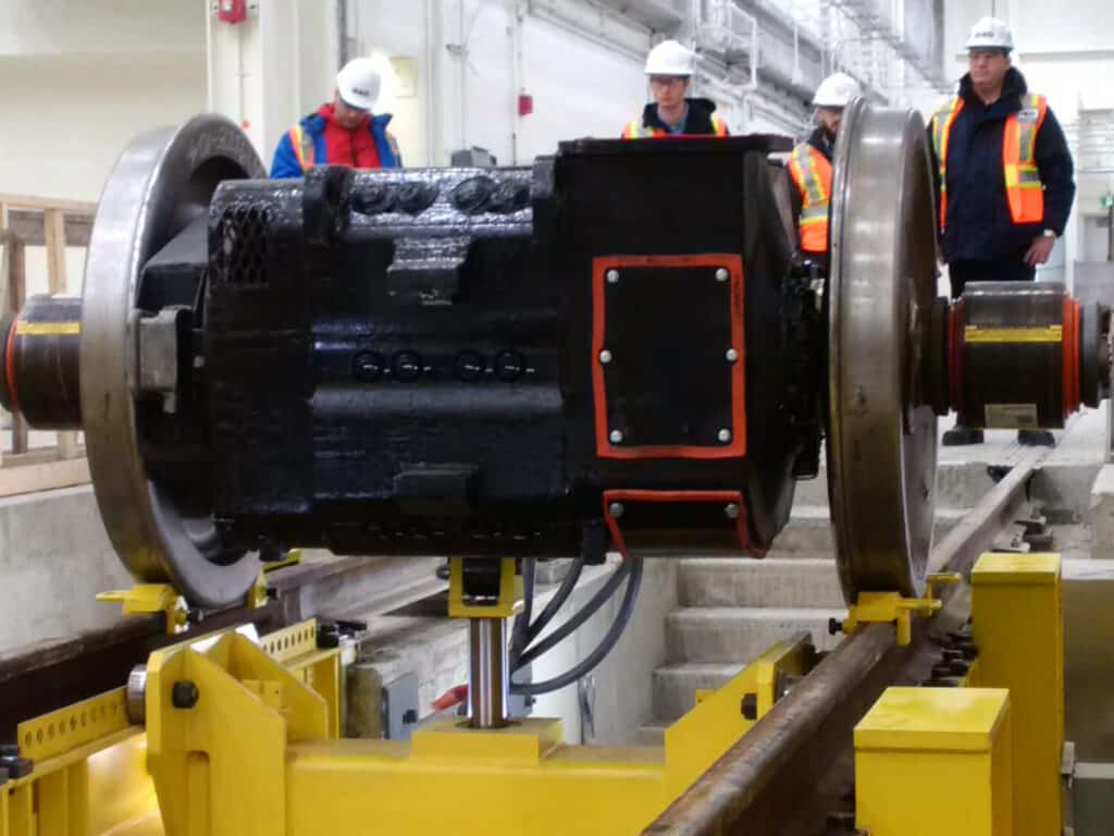 Railcar maintenance equipment with workers examining a train wheelset.