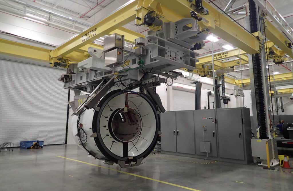 Lifting system hoisting large circular aerospace part in facility.