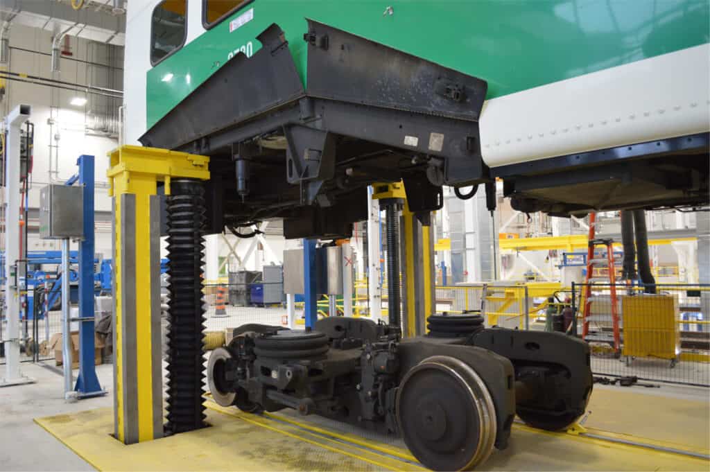 Railcar lifted above its bogie assembly by a yellow maintenance lift