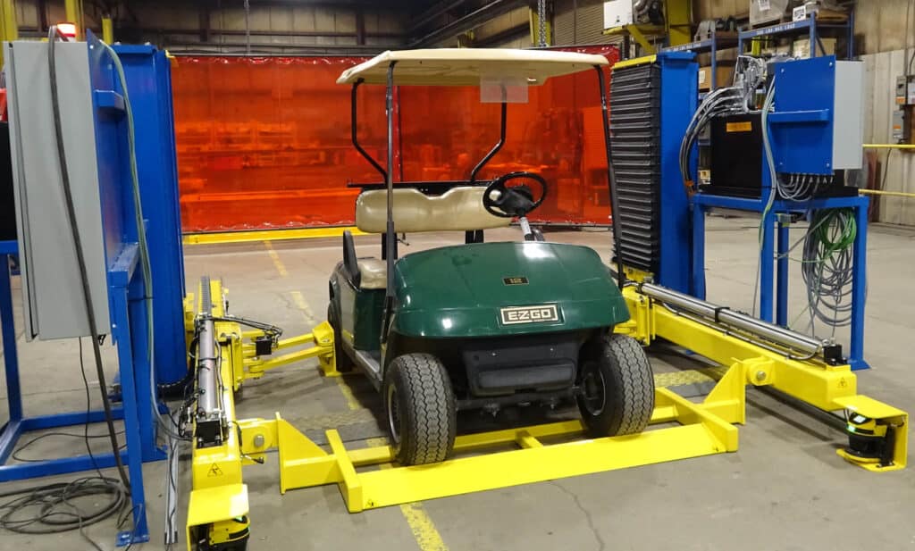 A golf cart mounted on a yellow unloader lift in an industrial warehouse setting.
