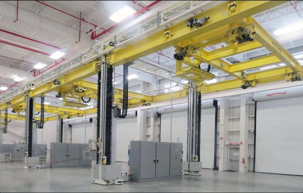 Overhead industrial positioning equipment with yellow gantry and hoists in a clean facility.
