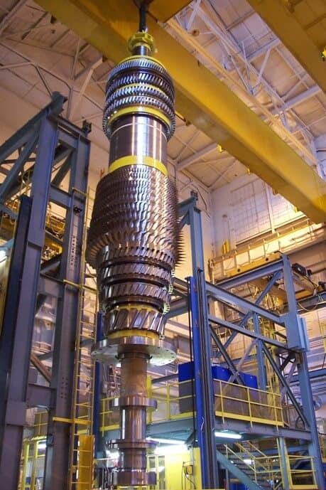 Turbine assembly held by a rig in an industrial plant with intricate metal components.