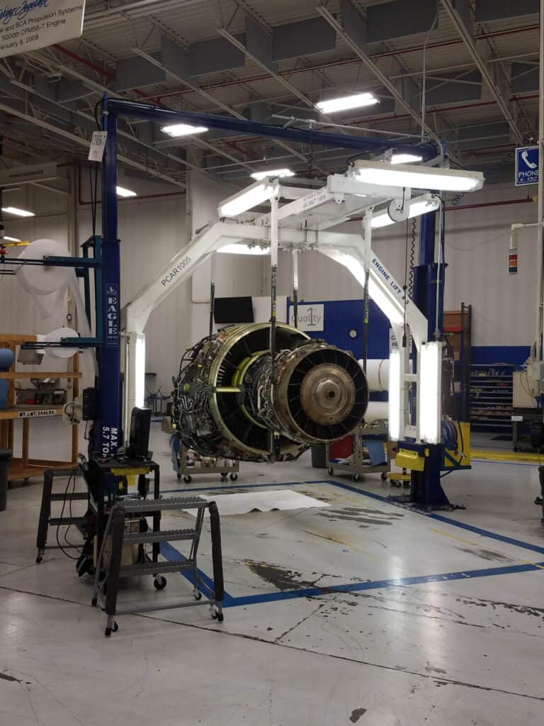 An aerospace engine suspended by a specialized lift system in an aerospace material handling facility.