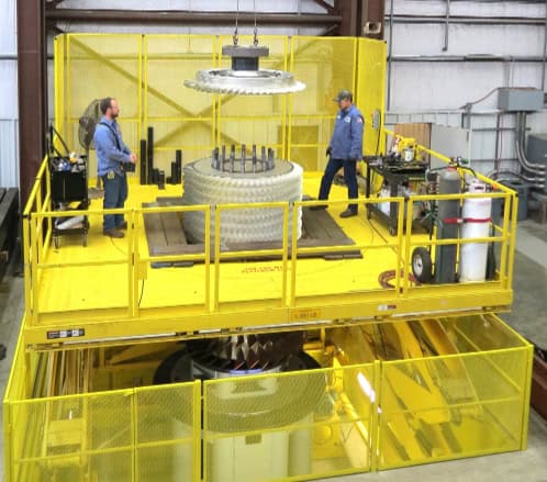 Two workers operate on a large, yellow custom personnel lift platform inside an industrial facility. The platform features guardrails and is elevated, with heavy machinery parts being handled. The lift is designed for safe and efficient access to high areas in industrial settings.