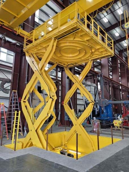 A yellow scissor lift platform in an industrial facility designed for custom personnel lifts.