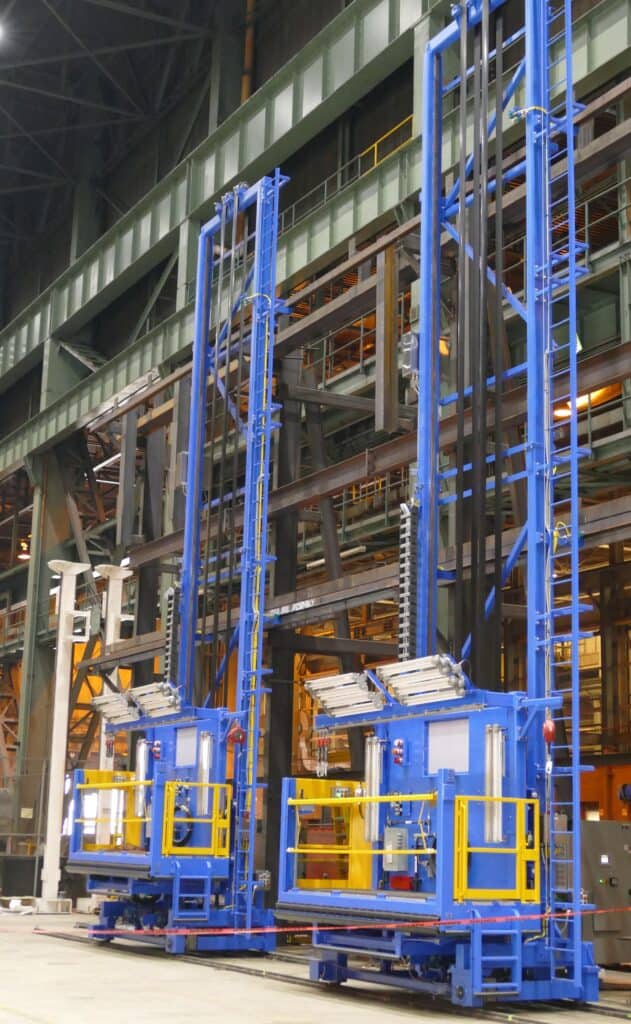 Two tall blue industrial lift platforms in a large facility, used for high-reaching tasks.